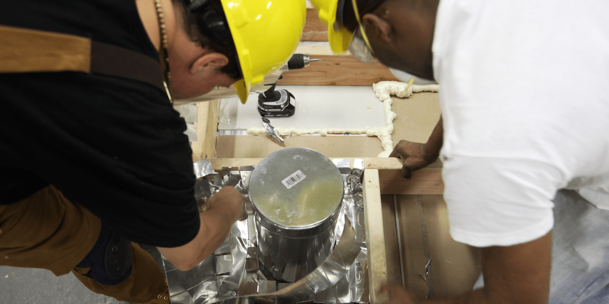 Trainees air sealing a flue chase with heat-resistant material during weatherization training