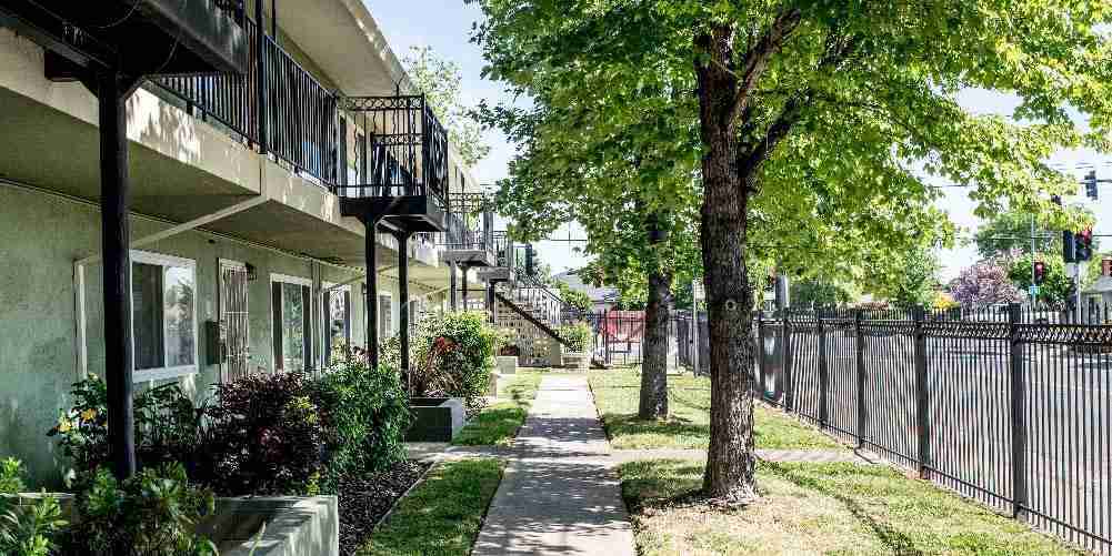 Multifamily residential housing development with landscaped walkways, mature trees, and energy-efficient apartment buildings.
