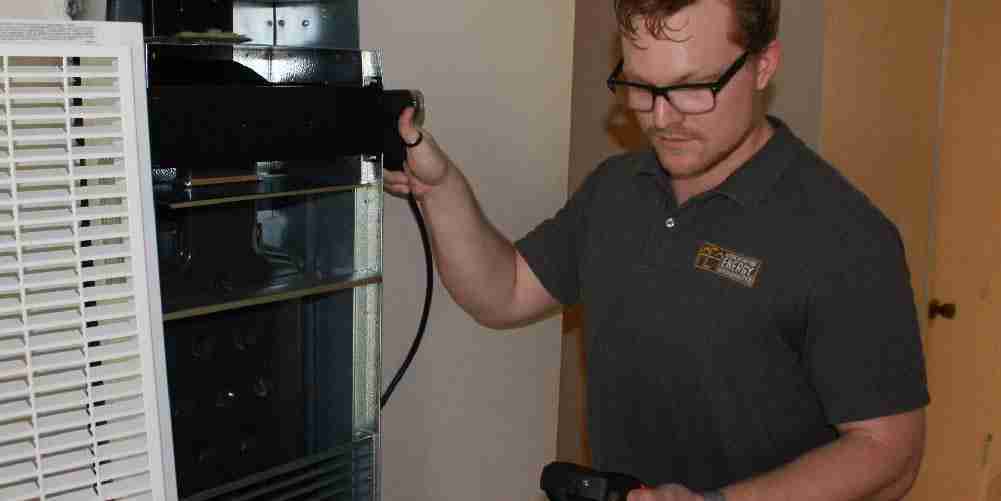 Technician performing an inspection of a wall furnace using diagnostic equipment during a residential energy efficiency assessment.