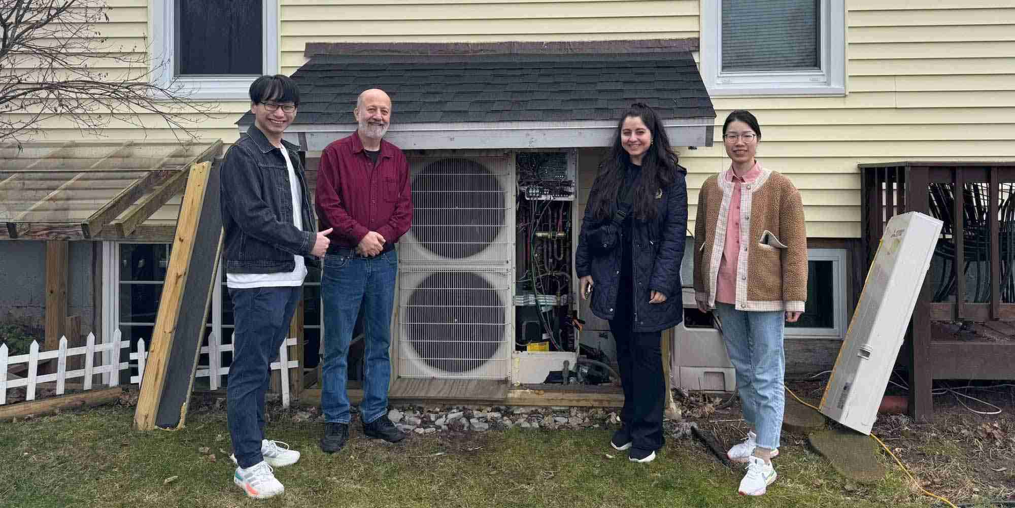 Group standing beside outdoor heat pump system installation at residential building